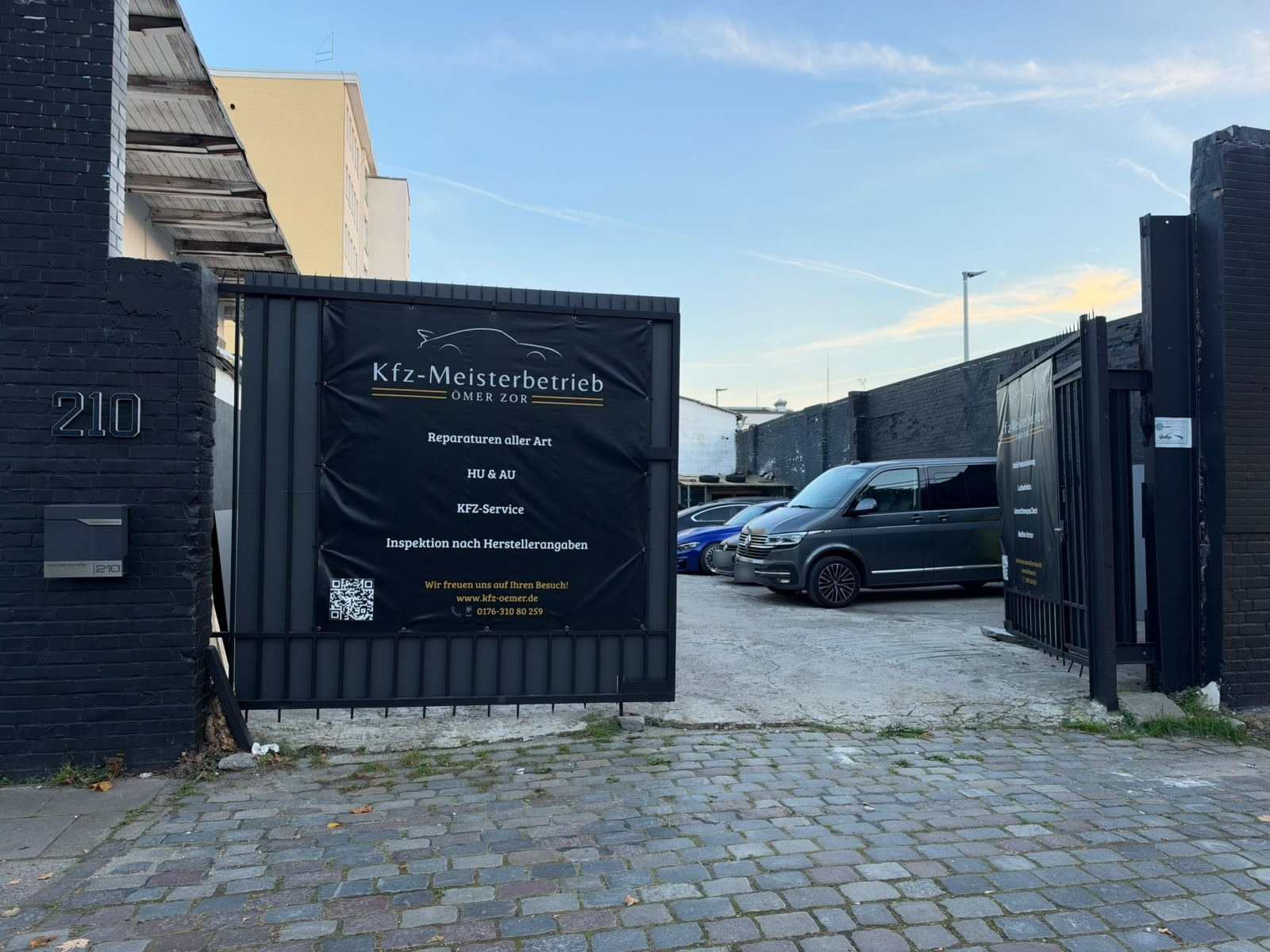 Einfahrt Wendenstraße 210: Hausnummer am schwarzen Pfeiler, offenes Tor mit dem Banner „Kfz-Meisterbetrieb Ömer Zor“, dahinter der Hof mit geparkten Autos